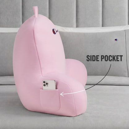 A Champion Jersey Backrest Pillow in pink rests on the bed. Made from soft jersey knit fabric, it has a handy side pocket for your smartphone—highlighted by the text “SIDE POCKET”—and is finished with an embroidered Champion logo.