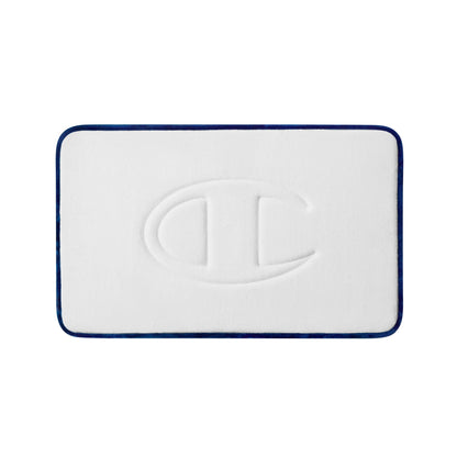 Introducing the Champion Quilted Logo Memory Foam Bath Mat: a white rectangular bath mat with a cushioned memory foam design, featuring a raised Champion “C” logo in the center and a dark blue border—perfect for adding both comfort and style to your bathroom.