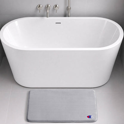 Modern white freestanding bathtub with chrome fixtures, set against gray tiled walls and floor. In front of the tub lies a light gray, skid-resistant Logo Patch Memory Foam Bath Mat from Champion, featuring a small Champion logo.