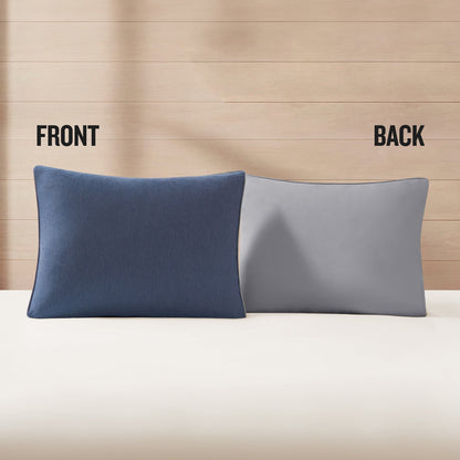 Two pillows from the Champion Reversible Solid Jersey Comforter Set are placed side by side on a bed against a wooden wall; the left pillow displays the dark blue front while the right pillow reveals the light gray back, emphasizing the reversible design with FRONT and BACK labels above each pillow.