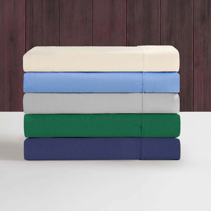 A neatly stacked set of five folded Champion Elastic Logo Microfiber Sheet Sets, in cream, light gray, light blue, green, and navy blue, rests on a white surface against a dark wood-paneled background.