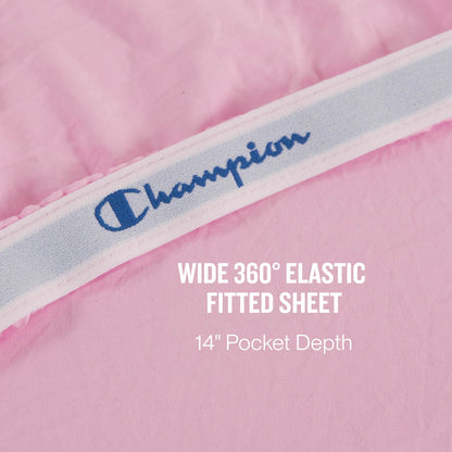A close-up of a pink Champion Peak Comfort Microfiber fitted sheet with a wide 360° elastic band showcases the athletic bedding, featuring text stating WIDE 360° ELASTIC FITTED SHEET 14” Pocket Depth. Part of the Champion Peak Comfort Microfiber Sheet Set, these deep pocket sheets ensure a secure and comfortable fit for your mattress.