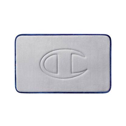 A light gray, rectangular Quilted Logo Memory Foam Bath Mat by Champion features rounded corners, dark blue edging, and a large embossed Champion “C” logo at the center. This stylish bath mat provides both comfort and a modern touch to your bathroom space.