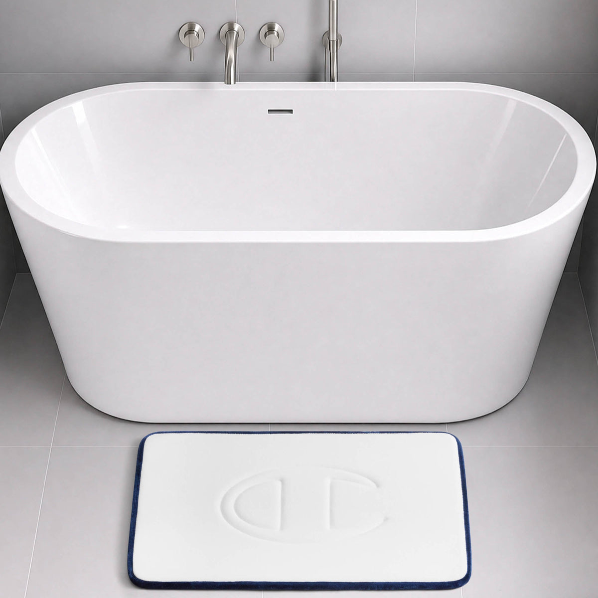 A modern white bathtub with a wall-mounted faucet, and a rectangular Champion Quilted Logo Memory Foam Bath Mat, offering cushioned comfort, placed on a gray tiled floor.