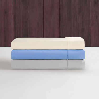 Three neatly folded bed sheets from the Champion Elastic Logo Microfiber Sheet Set in cream, blue, and light gray are stacked on a white surface, showcasing their soft microfiber fabric with Champion’s signature elastic logo detail, all set against a dark wooden panel background.