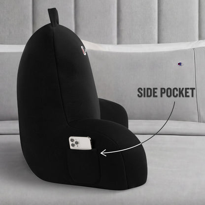 A Champion Jersey Backrest Pillow in black is displayed on a bed with gray pillows, showcasing its iconic logo and a handy side pocket holding a smartphone. An arrow points to the pocket with the label “SIDE POCKET,” emphasizing this pillow’s functional design.
