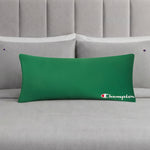A green Champion Jersey Body Pillow, adding an athletic touch, rests on a neatly made bed with gray sheets and matching Champion-branded pillowcases, all set against a gray upholstered headboard.
