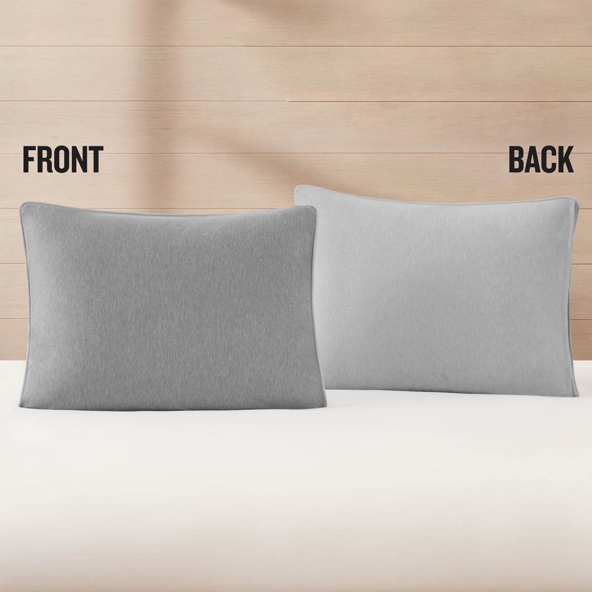 Two gray pillows are displayed on a bed, one labeled FRONT and the other BACK, set against a light wooden wall background—perfect for pairing with an athletic bedding look like the Champion Premium Reversible Solid Jersey Comforter Set.