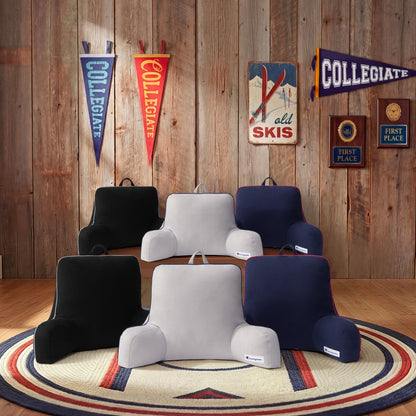 Six Champion Faux Wool Backrest Pillows in black, gray, and navy are arranged on a circular rug in a rustic room featuring wooden walls, sports pennants, and vintage ski decor.
