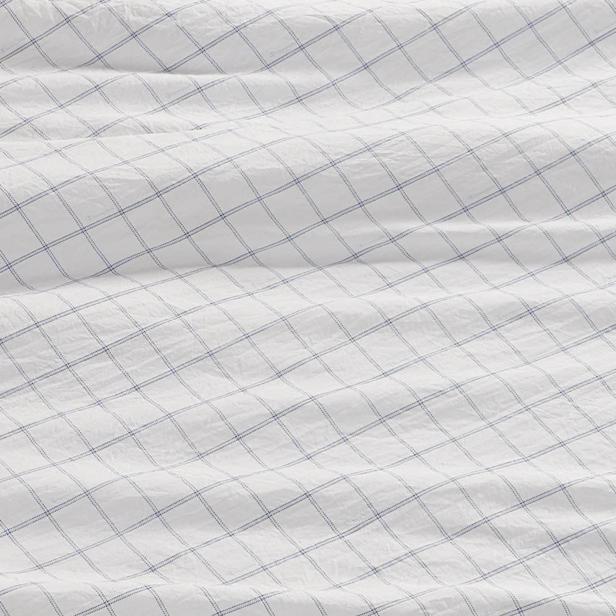 A close-up of a white fabric with a blue grid pattern, slightly wrinkled and textured, shows intersecting thin blue lines—these Champion Printed Microfiber Sheet Sets deliver both everyday comfort and stylish printed design.