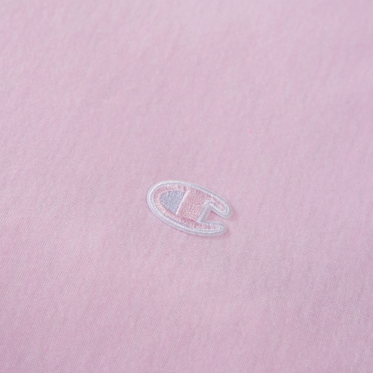 Close-up of a light pink fabric with a small, white embroidered C logo near the center, representing the Champion brand—an ideal accent for those looking to add a stylish touch to their Champion Reversible Solid Jersey Comforter Set.