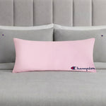 A Champion Jersey Body Pillow in pink is centered on a neatly made bed with gray bedding and matching pillows, each pillowcase adorned with small Champion logos. This cozy accent from Champion adds sporty flair to the room, making it perfect for fans of the brand.