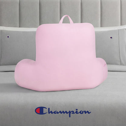 A pink Champion Jersey Backrest Pillow with armrests sits on a gray bed dressed in soft jersey knit bedding, featuring Champion logos on the pillows and headboard, with a large Champion logo displayed at the foot of the bed.