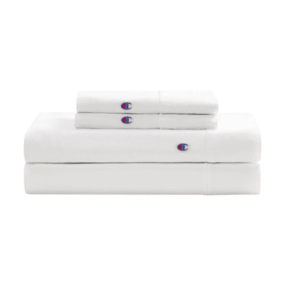 A neatly folded Embroidery Patch Microfiber Sheet Set by Champion, including two pillowcases and two sheets, each accented with a small blue and red embroidered Champion patch for an athletic-inspired bedding look.