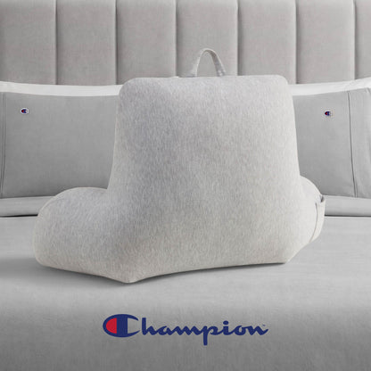 A Champion Jersey Backrest Pillow in light gray with armrests sits on a bed dressed in cozy gray jersey knit bedding. The Champion logo is featured on both the pillowcases and at the foot of the bed, bringing a signature Champion style to the room.